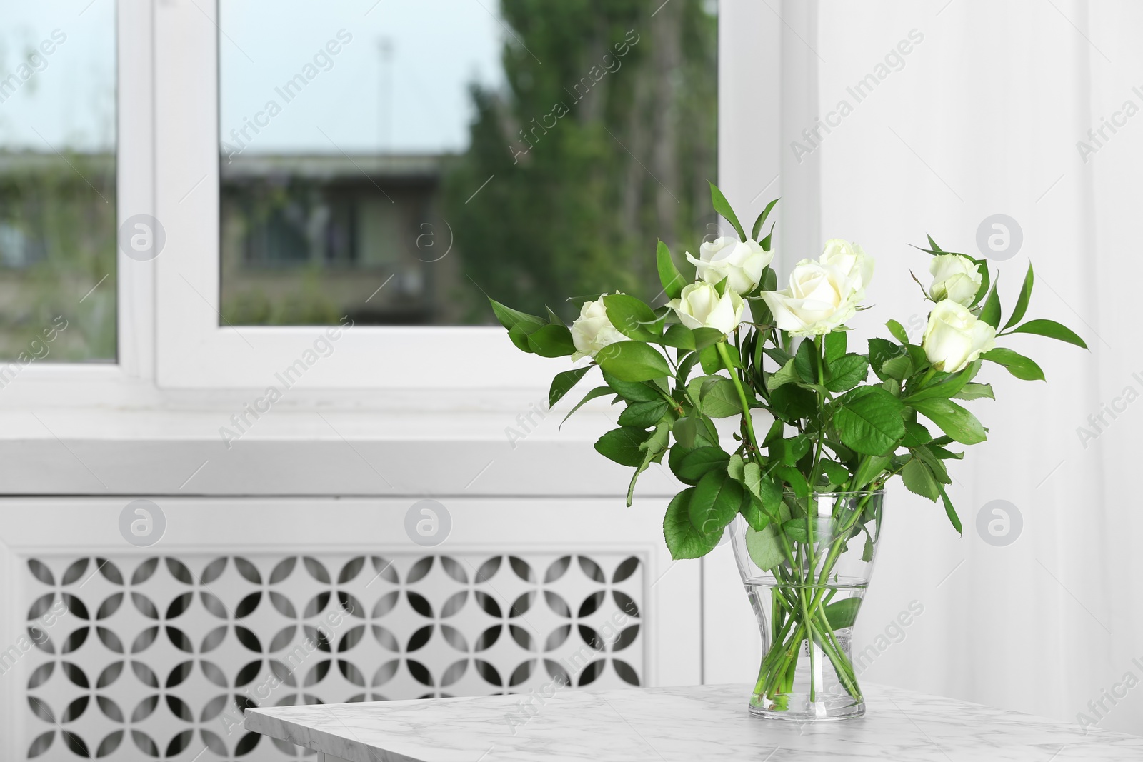 Photo of Glass vase with bouquet of beautiful roses on table in room. Space for text