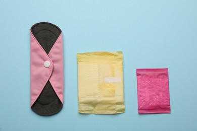 Photo of Disposable menstrual pads near reusable cloth one on light blue background, flat lay
