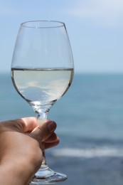 Woman holding glass with wine near sea, closeup