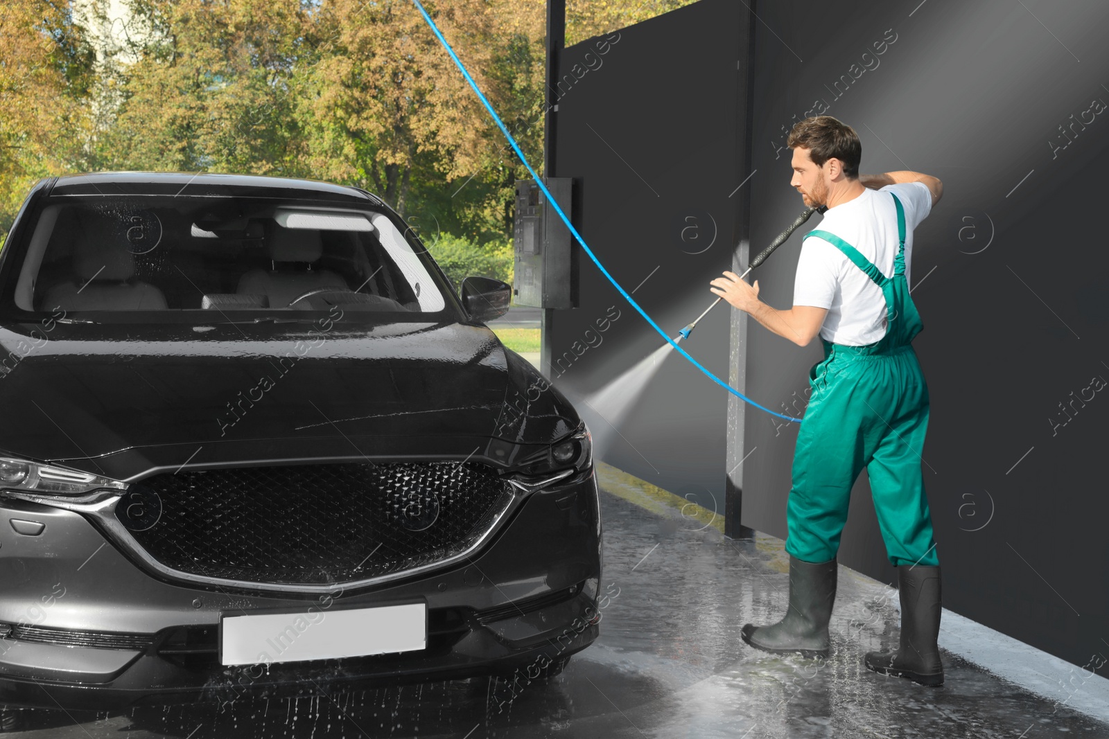 Photo of Worker washing auto with high pressure water jet at outdoor car wash