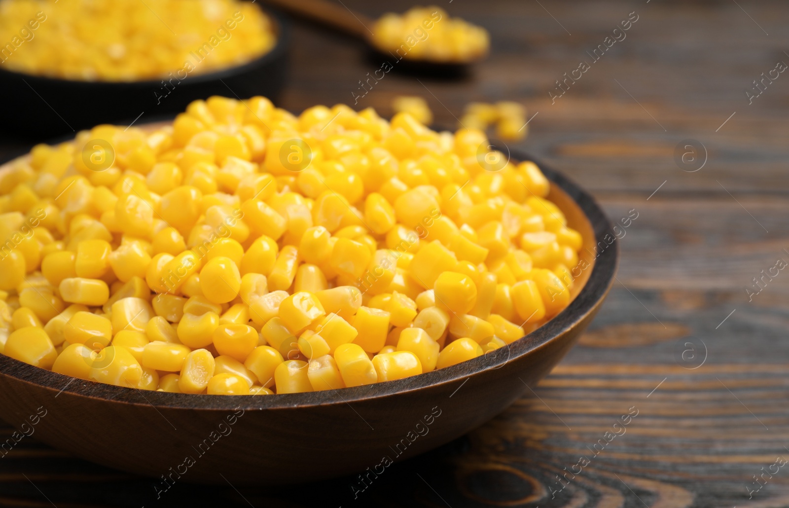 Photo of Delicious canned corn in bowl on wooden table, closeup