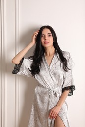 Photo of Pretty young woman in beautiful silk robe near white wall