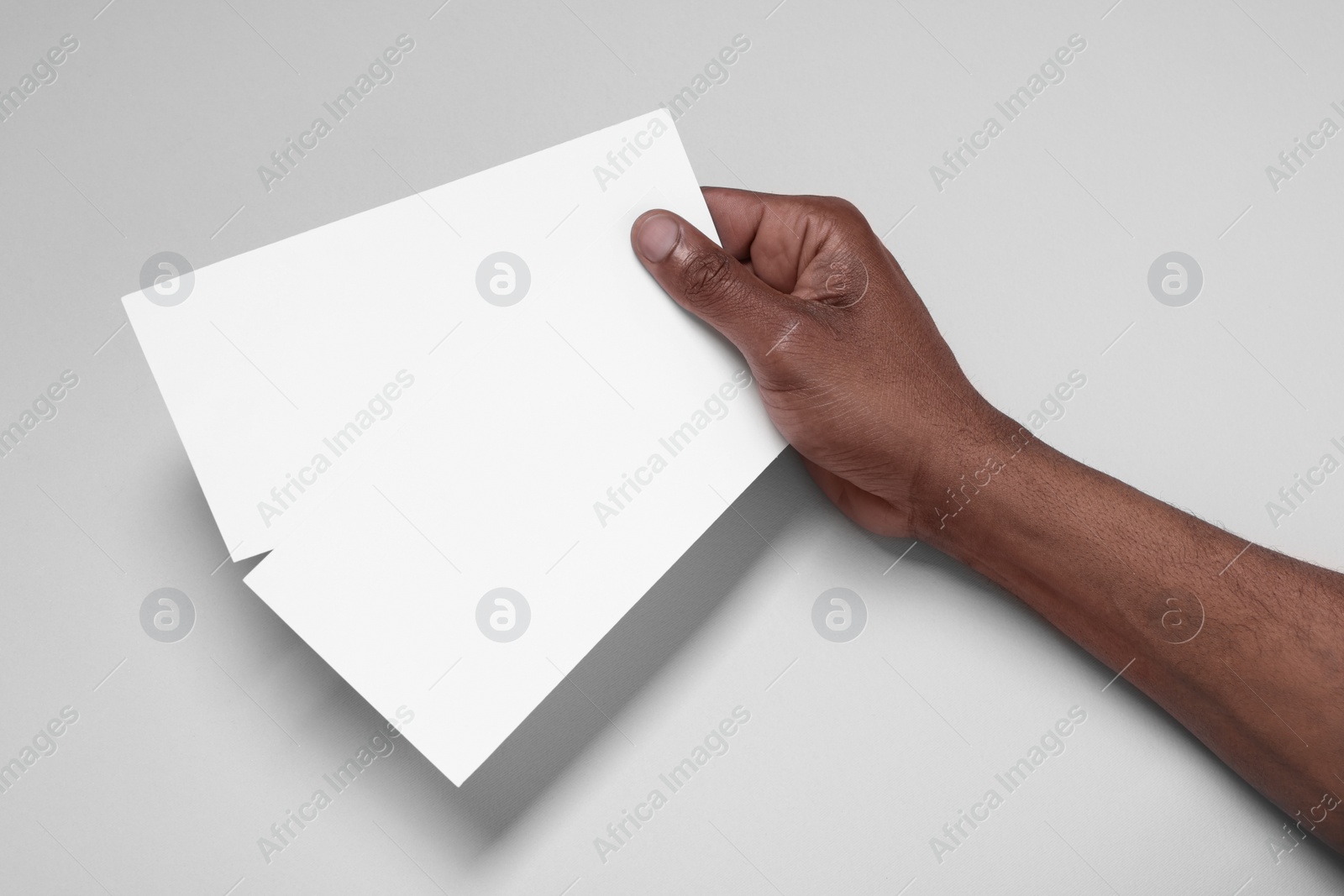 Photo of African American man holding flyers on white background, closeup. Mockup for design