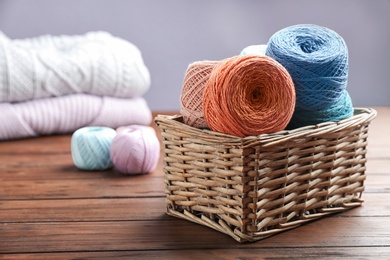 Photo of Colorful clews of threads in wicker basket on wooden table, space for text