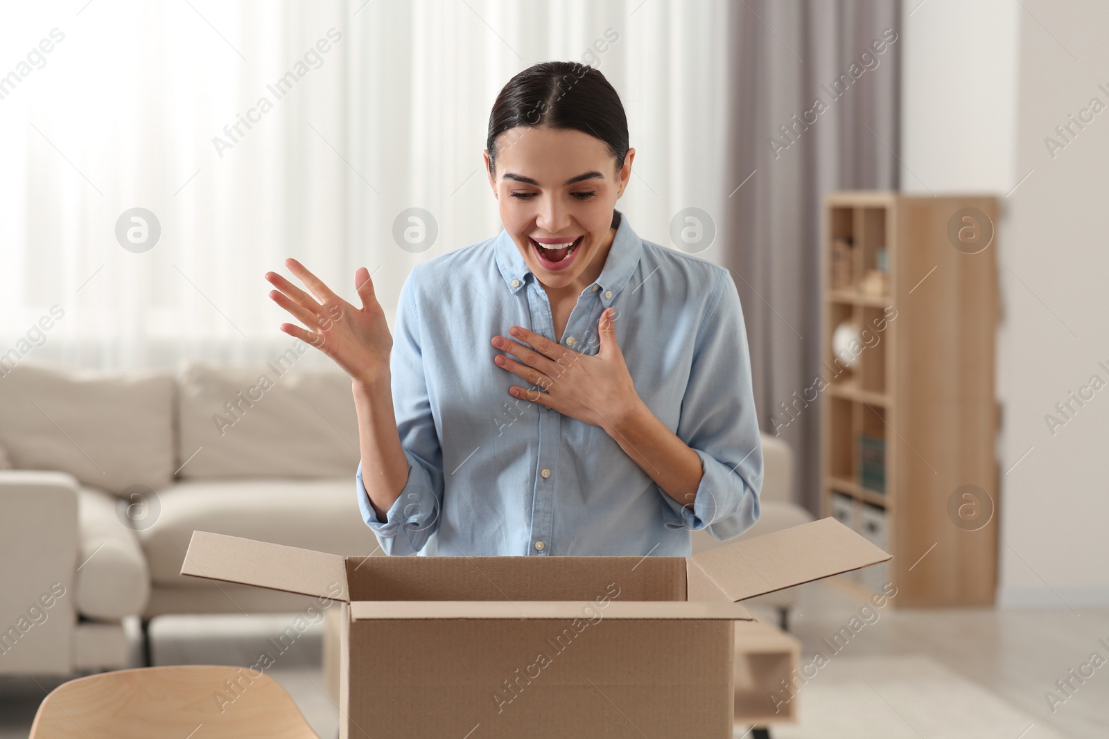 Photo of Emotional young woman with opened parcel at home. Internet shopping