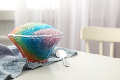 Photo of Rainbow shaving ice in glass dessert bowl and spoon on white table indoors