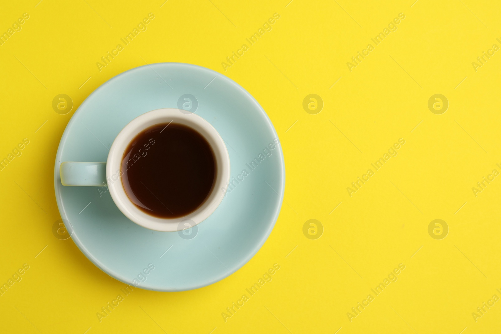 Photo of Tasty coffee in cup on yellow background, top view. Space for text