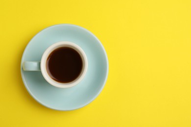 Photo of Tasty coffee in cup on yellow background, top view. Space for text