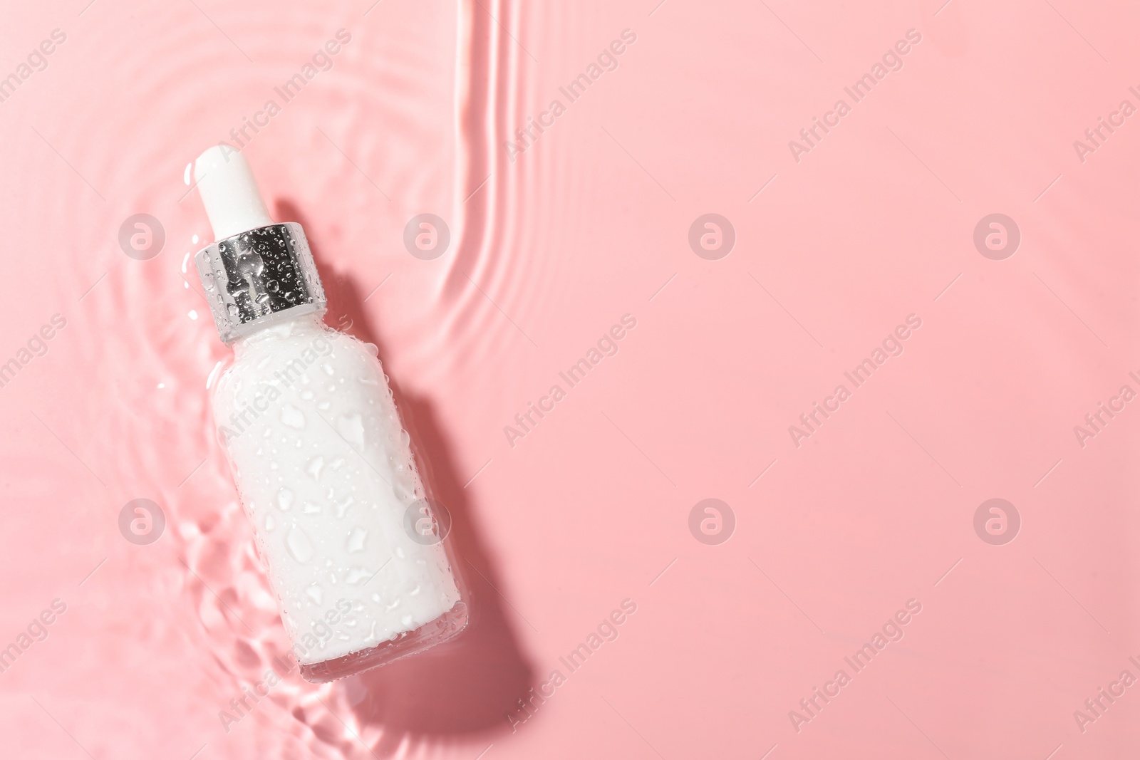 Photo of Bottle of cosmetic product in water on pink background, top view. Space for text