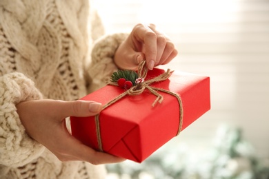 Woman holding red Christmas gift box indoors, closeup