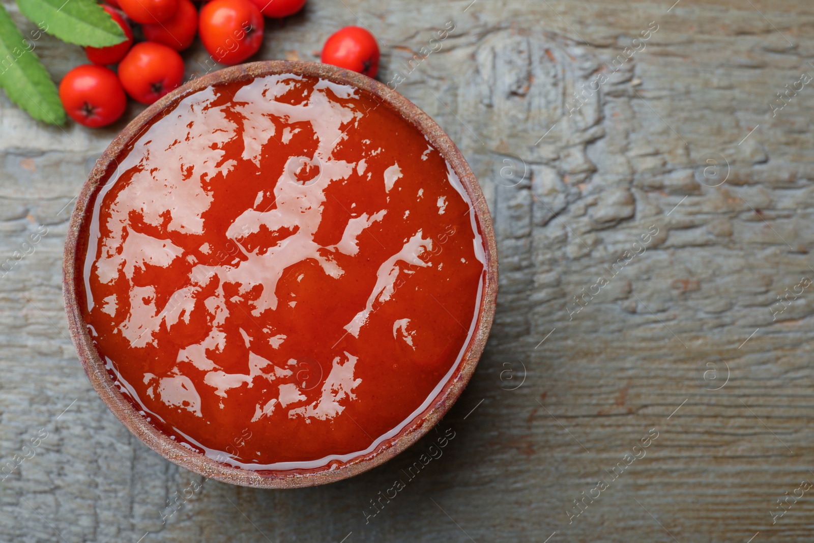 Photo of Delicious rowan jam and berries on wooden table, flat lay. Space for text