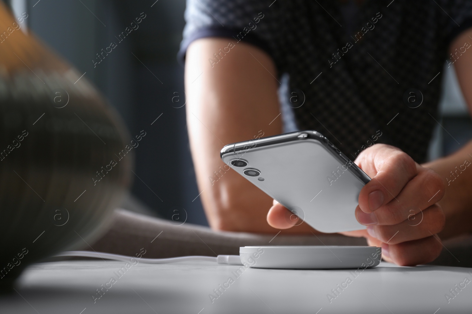 Photo of Man putting smartphone on wireless charger in room, closeup