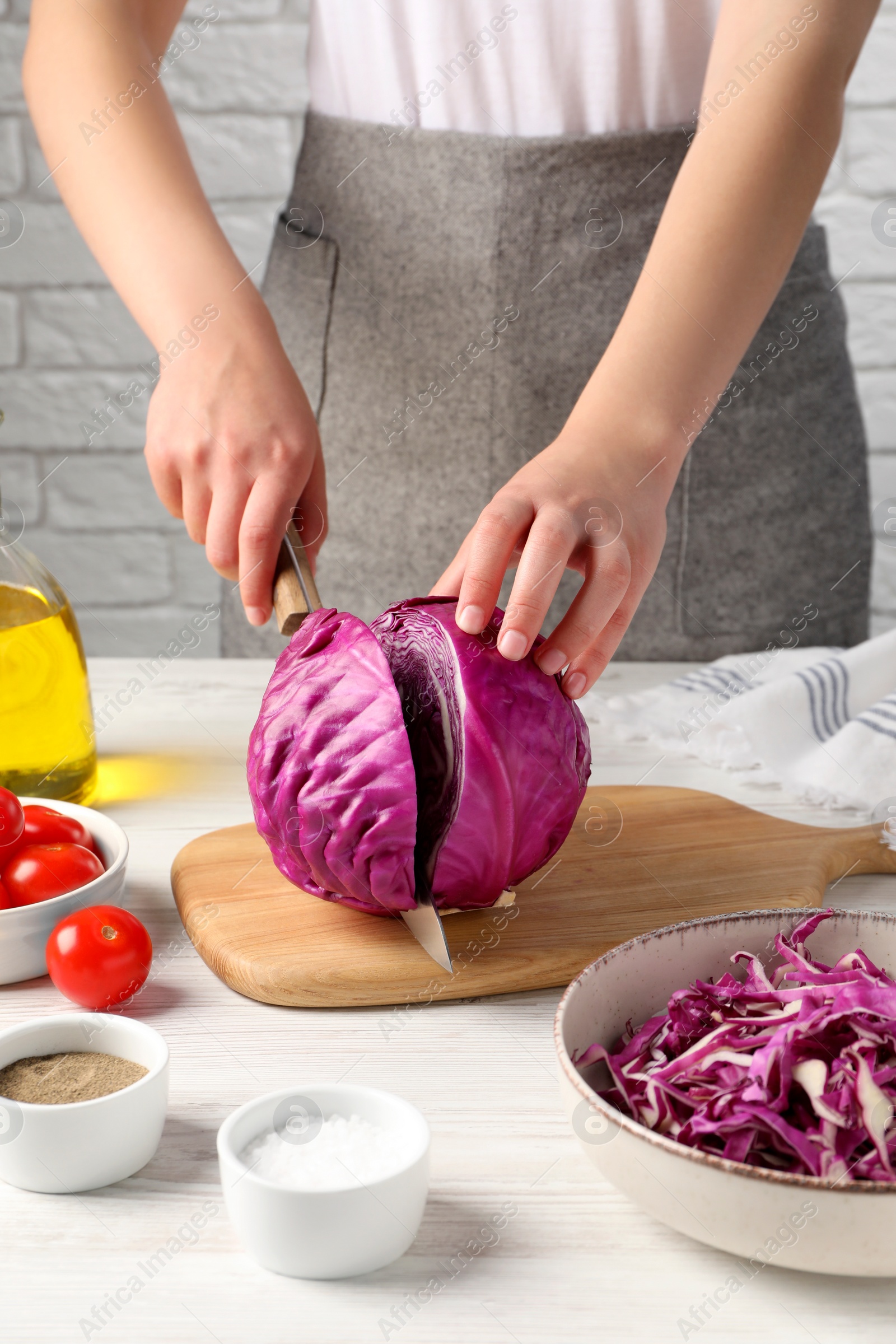 Photo of Woman cutting fresh red cabbage at white wooden table, closeup