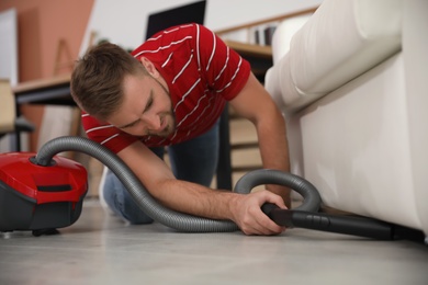 Young man using vacuum cleaner in living room