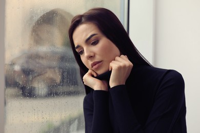 Photo of Depressed woman near window on rainy day