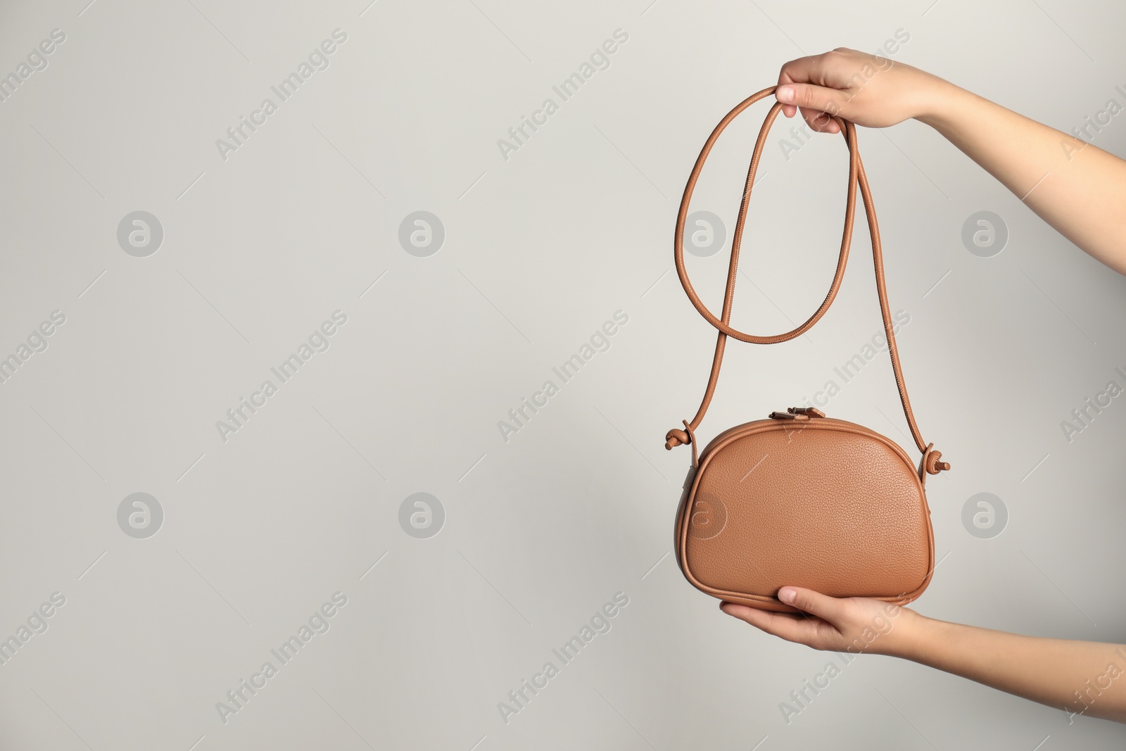 Photo of Woman holding stylish bag on light background, closeup. Space for text