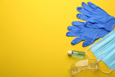 Flat lay composition with medical gloves, masks and hand sanitizer on yellow background. Space for text