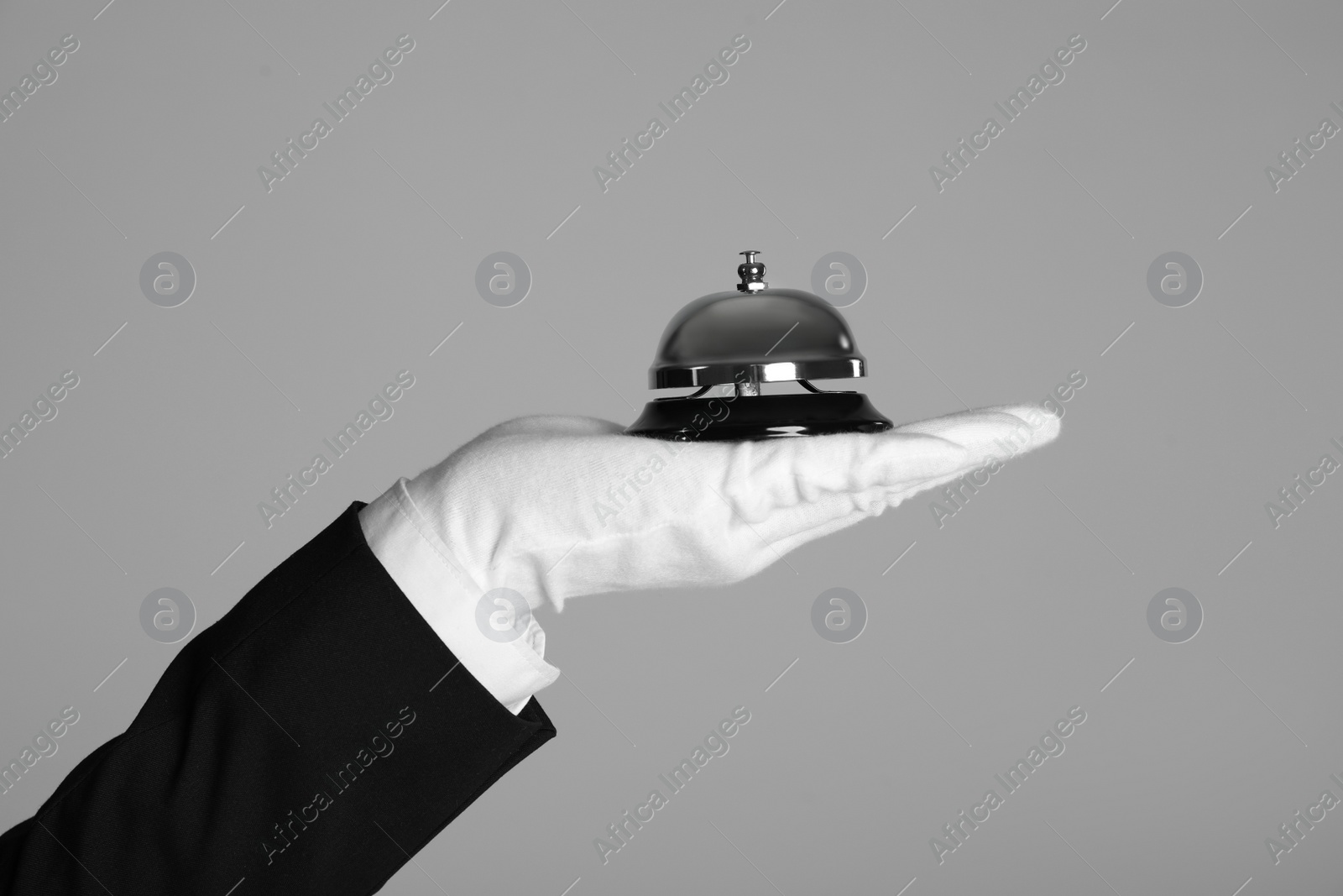 Photo of Butler holding service bell on grey background, closeup