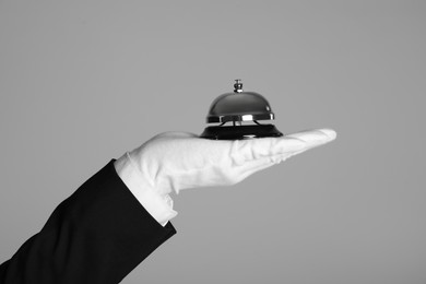 Photo of Butler holding service bell on grey background, closeup
