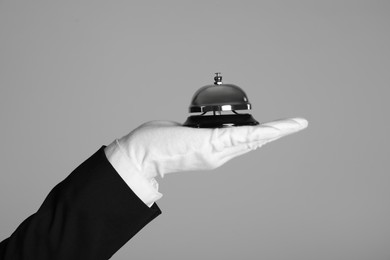 Butler holding service bell on grey background, closeup