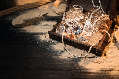 Photo of Chest with treasures and scattered sand on wooden floor, above view. Space for text