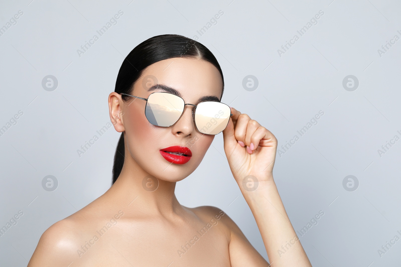 Image of Attractive woman in stylish sunglasses on light grey background. Sky with clouds reflecting in lenses. Space for text