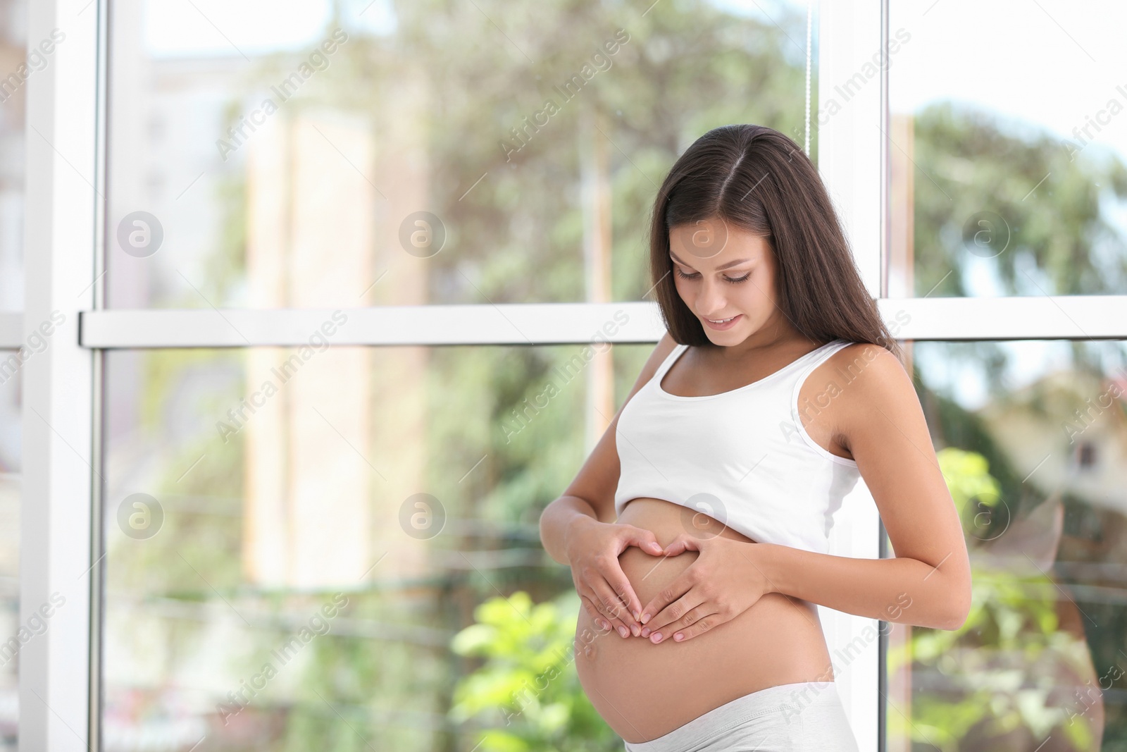 Photo of Happy pregnant woman standing near window at home