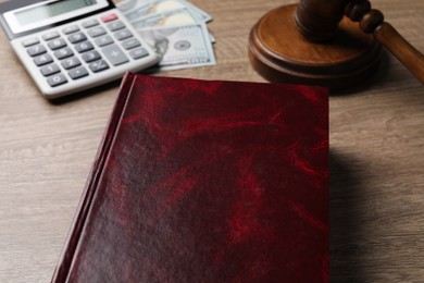 Tax law. Book, calculator, dollar banknotes and gavel on wooden table, closeup