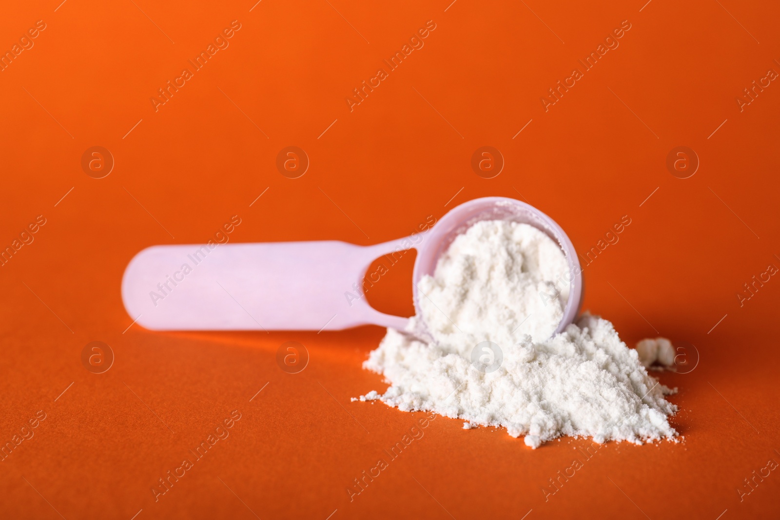 Photo of Scoop and scattered protein powder on orange background