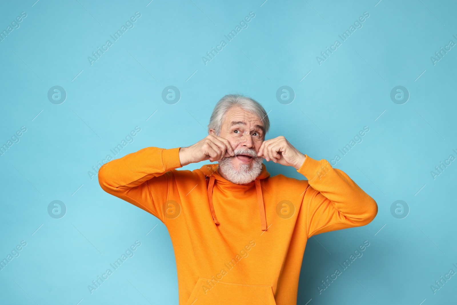 Photo of Senior man touching mustache on light blue background