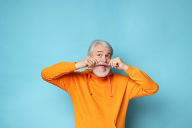 Photo of Senior man touching mustache on light blue background