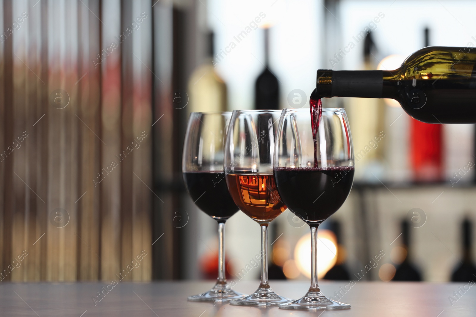 Photo of Pouring red wine from bottle into glass on table indoors, space for text