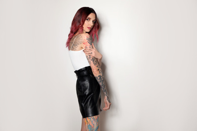 Photo of Beautiful woman with tattoos on body against light background