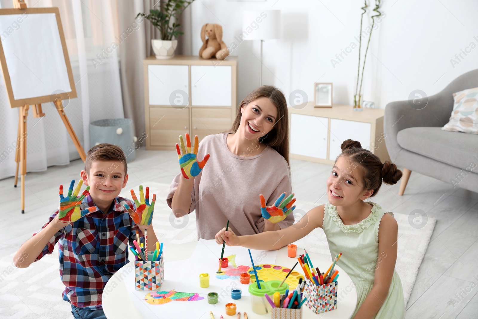 Photo of Cute children and young woman with painted hands at table indoors