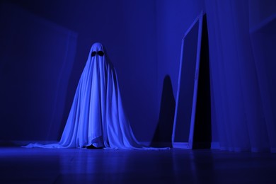 Photo of Creepy ghost. Woman covered with sheet in blue light, low angle view