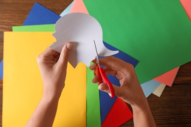 Photo of Woman cutting white paper with scissors at wooden table, top view