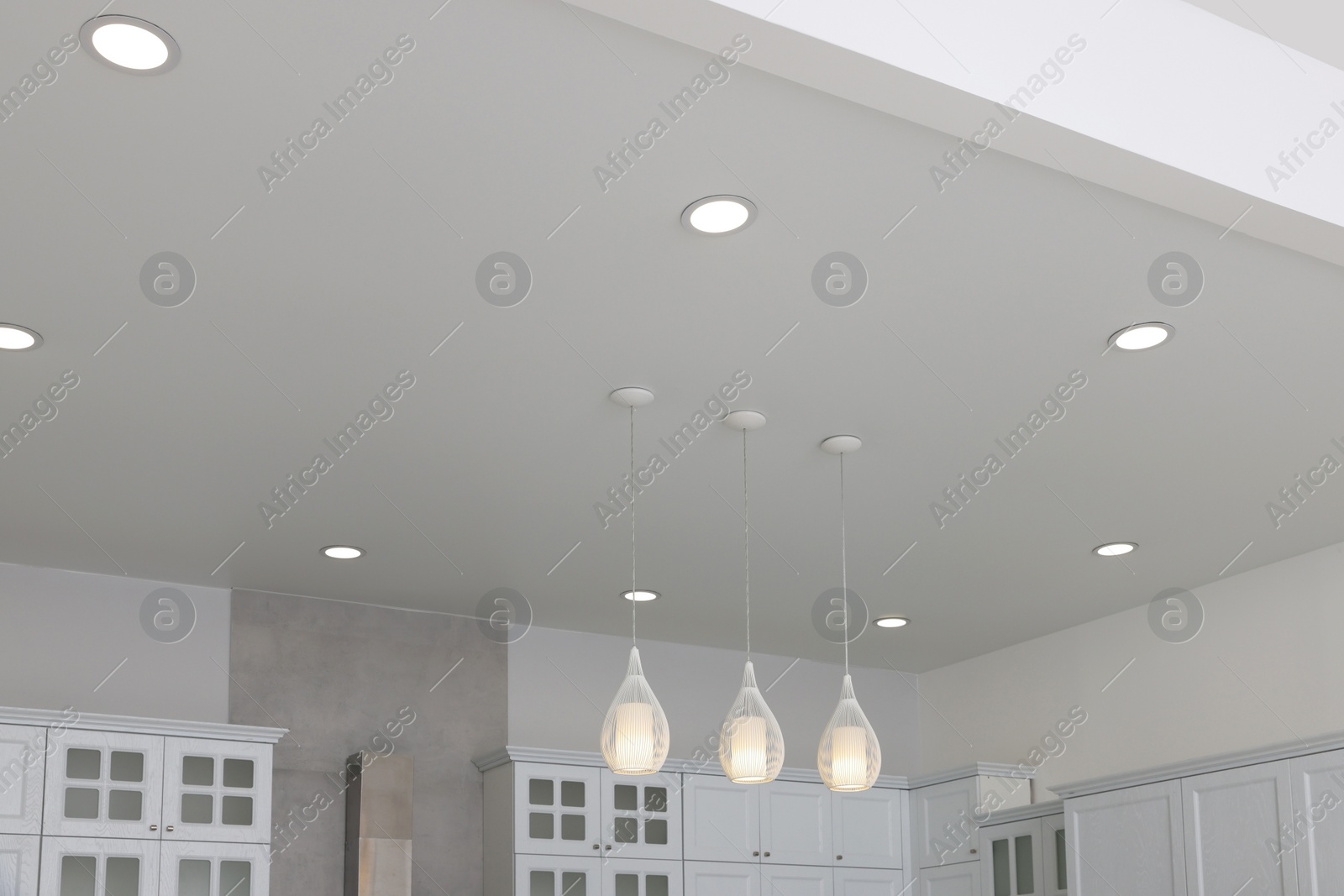 Photo of Ceiling with modern lamps, furniture and cooker hood in stylish kitchen, low angle view