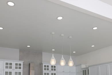 Photo of Ceiling with modern lamps, furniture and cooker hood in stylish kitchen, low angle view