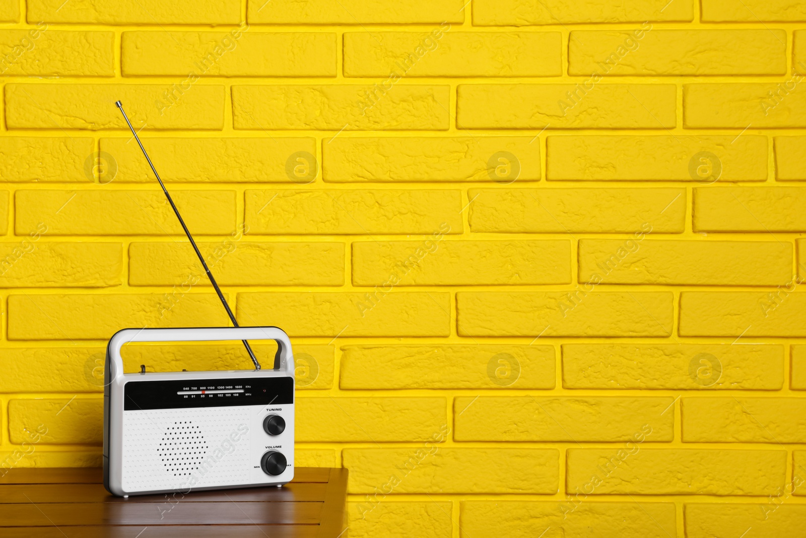 Photo of Retro radio receiver on wooden table near yellow brick wall. Space for text