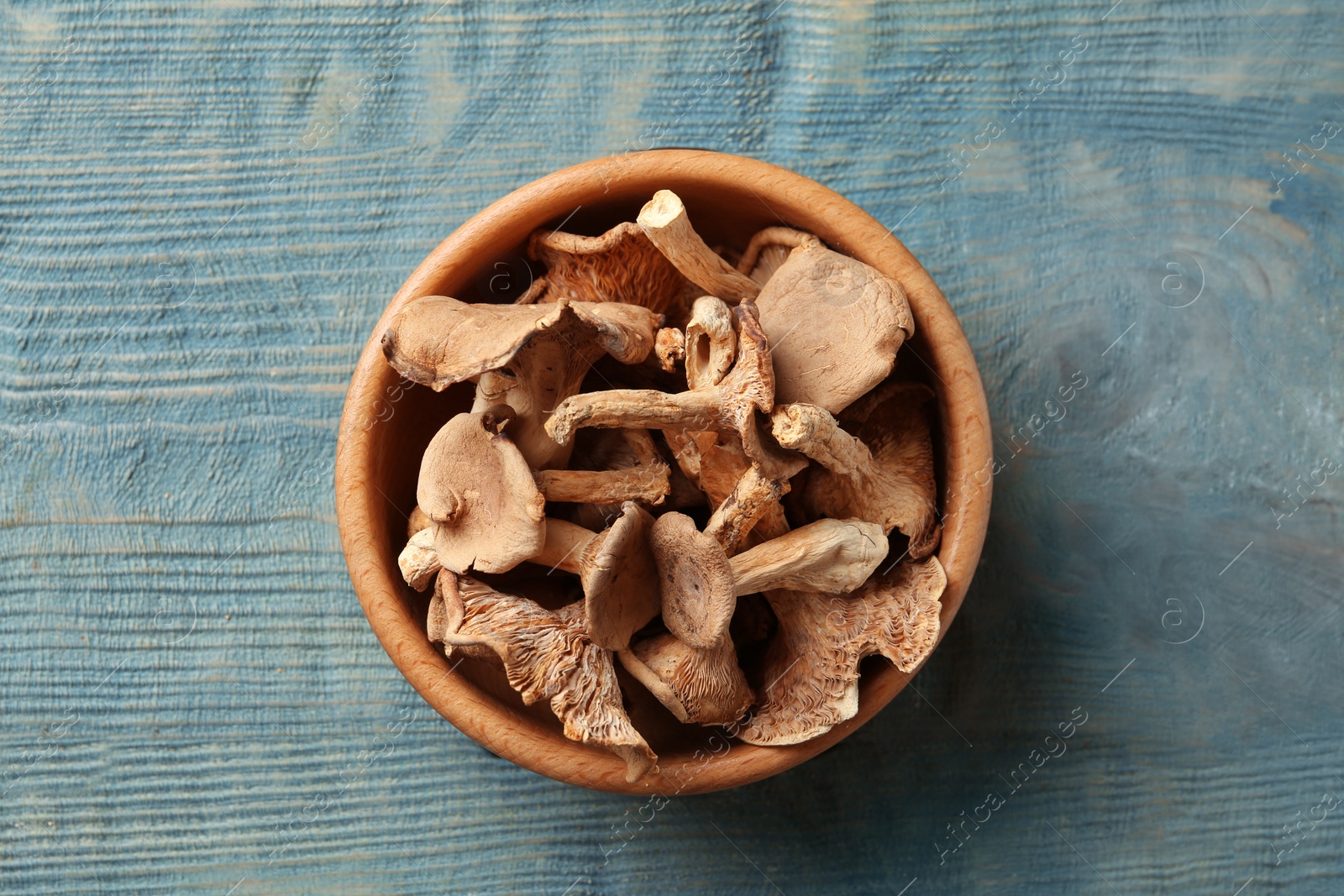 Photo of Bowl of dried mushrooms on color wooden background, top view