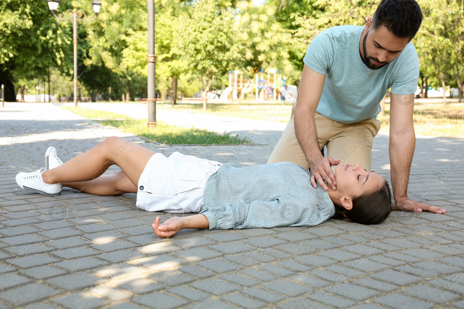Photo of Young man checking pulse of unconscious woman outdoors. First aid