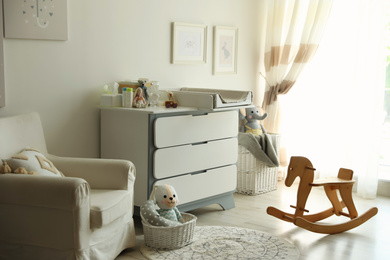 Photo of Beautiful baby room interior with toys, armchair and modern changing table