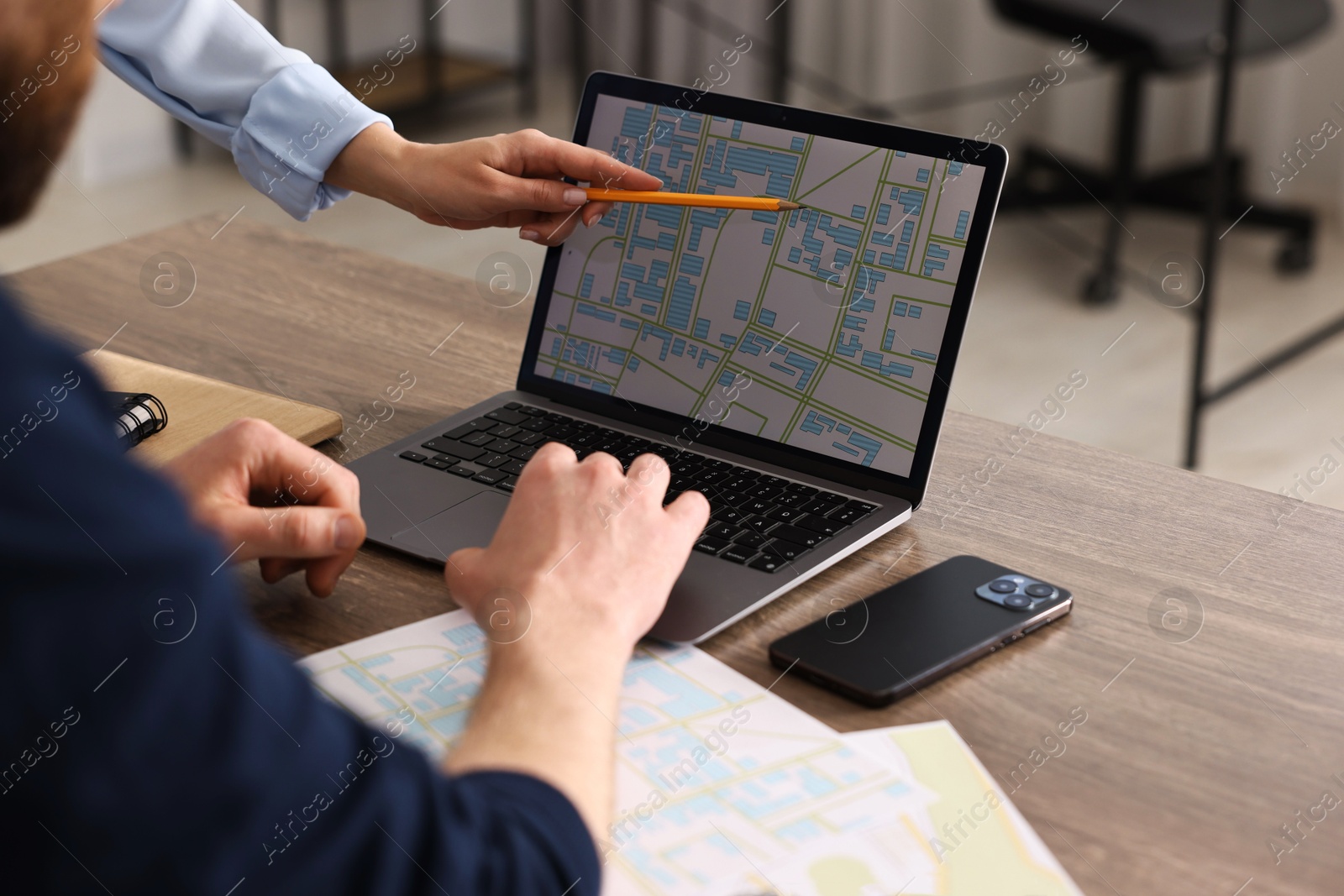 Photo of Cartographers working with cadastral map on laptop at wooden table in office, closeup