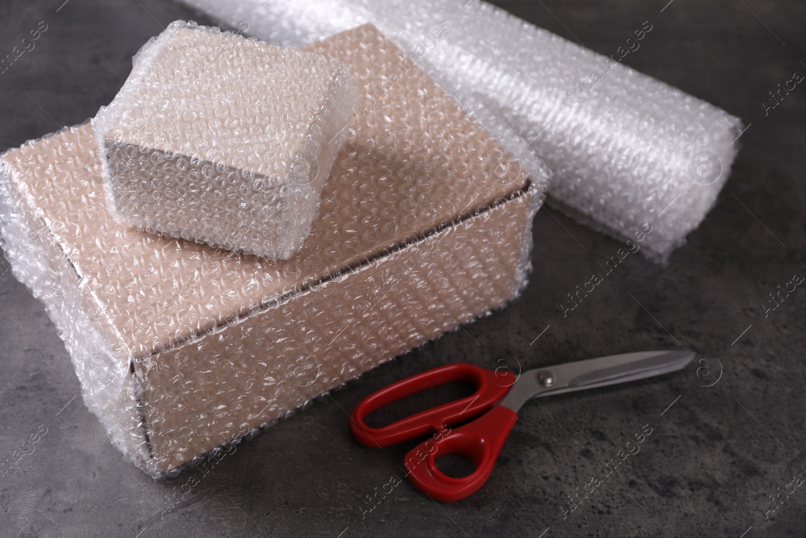 Photo of Cardboard boxes, bubble wrap and scissors on dark grey table