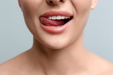 Woman licking her lips on light background, closeup