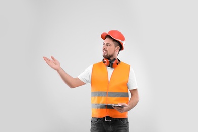 Photo of Male industrial engineer in uniform with clipboard on light background. Safety equipment