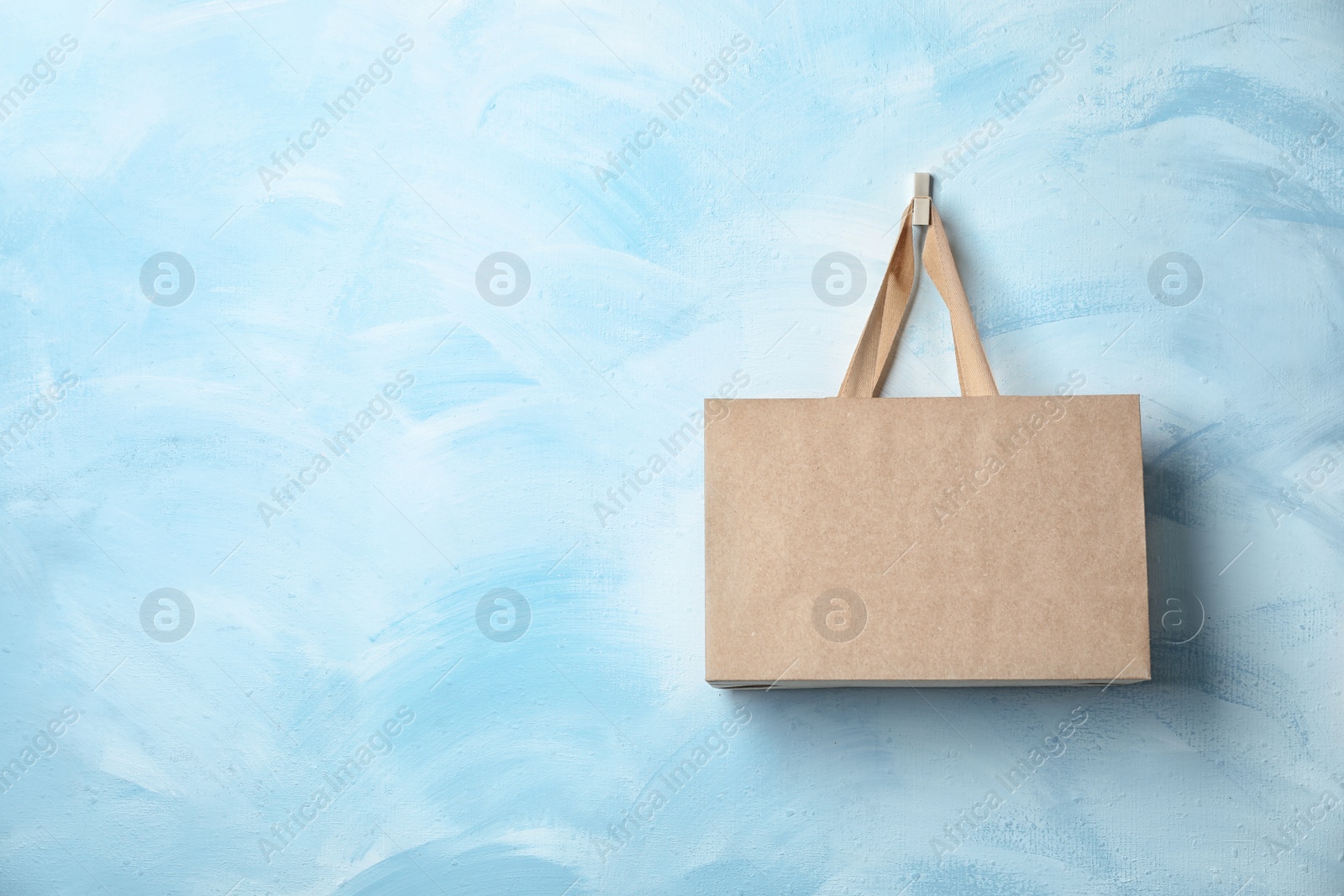 Photo of Paper shopping bag with comfortable handles hanging on color wall. Mockup for design