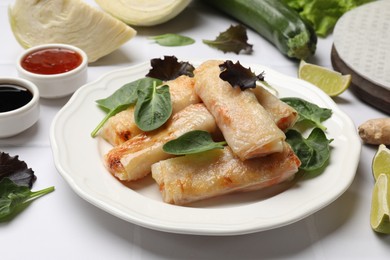 Plate with tasty fried spring rolls and spinach on white tiled table, closeup