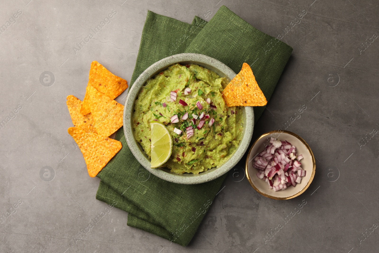 Photo of Bowl of delicious guacamole, nachos chips and lime on grey table, flat lay