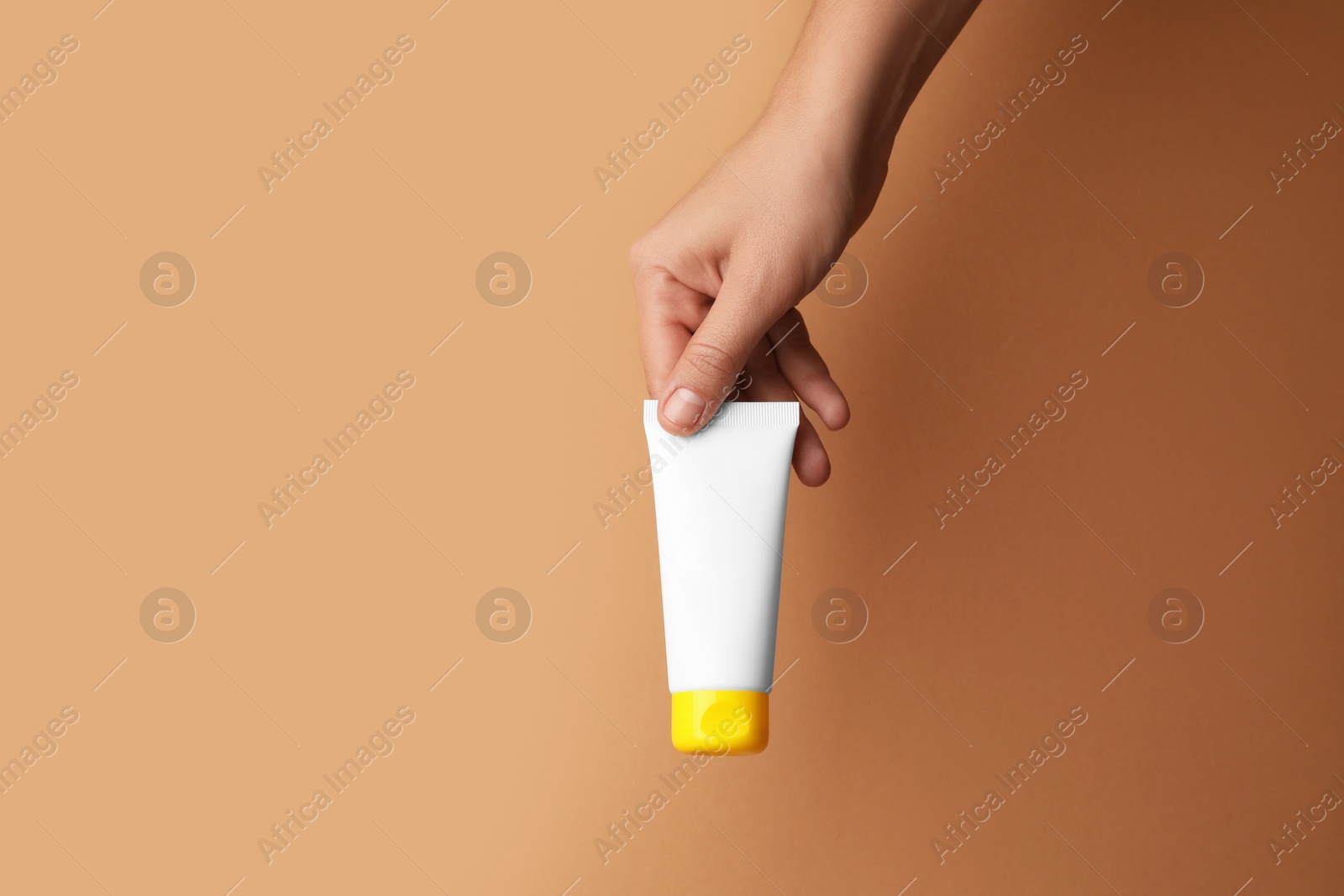 Photo of Woman holding tube of face cream on beige background, closeup. Space for text